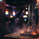 A chrome model rocket above an arcade launch platform, with a glowing gaming cabinet in a dark neon-lit lounge