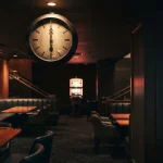 Unnumbered vintage clock at midnight in a warmly lit dark lounge, with a glowing slot machine in the background