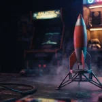 Small model rocket poised on a dark tabletop with an illuminated arcade cabinet in a warm neon gaming lounge