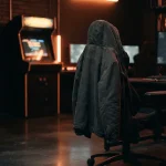 An unmarked dark coat draped over a chair in a neon-lit gaming lounge, with an arcade cabinet glowing behind it