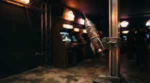 A small rocket on a launch rail in a dark amusement hall, with a warmly glowing arcade machine behind it
