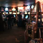 A rocket-shaped arcade attraction under warm neon lights, with a slot cabinet in a dark gaming lounge behind it
