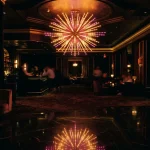 Glowing starburst chandelier over a dark casino lounge with a softly lit slot machine in the background