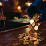Golden coins spilling beside a vintage arcade machine in a dark neon-lit gaming lounge with a softly glowing game table