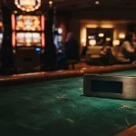 An unbranded hardware crypto wallet resting on a dark casino table with a softly glowing slot cabinet beyond