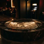 A dramatic whirlpool turning inside a polished indoor fountain, with a warmly glowing arcade cabinet in the background