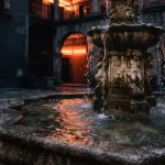 Illuminated stone fountain in a dark courtyard with warm neon reflections and a softly lit arcade cabinet behind it