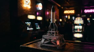 A polished model rocket on an arcade launch platform, with a softly glowing slot cabinet behind it in a dark neon lounge