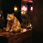 A realistic golden panda sculpture among bamboo in a dark neon-lit lounge, with a vintage slot machine behind it