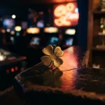 A brass four-leaf clover charm on a dark arcade counter with softly glowing game tables behind it
