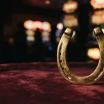 A polished golden horseshoe on a velvet casino lounge table, with warm neon lights and a slot machine softly blurred behind it