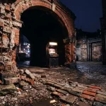 Partly demolished brick arcade arch in a dark courtyard, with warm neon lighting and a vintage game cabinet nearby
