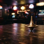 A polished metal spinning top turning on a dark gaming lounge table with a softly glowing arcade cabinet behind it