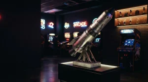 A model rocket poised for launch beside a glowing arcade cabinet in a dark, cinematic entertainment lounge