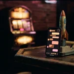 A glowing phone beside a miniature rocket arcade game and a softly lit gaming cabinet in a dark neon lounge