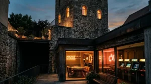 An illuminated stone watchtower above a dark arcade lounge with a softly glowing game table and warm neon lighting