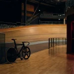 A racing bicycle beside an indoor velodrome with warm neon lighting and a small arcade lounge behind it