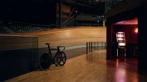 A racing bicycle beside an indoor velodrome with warm neon lighting and a small arcade lounge behind it